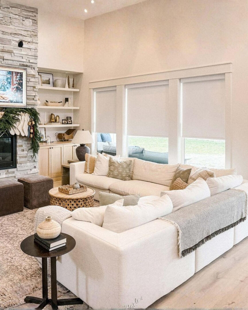 Modern frost linen blackout roller shades installed on three large windows behind a white sectional sofa in a bright, decorated living room.